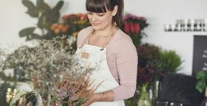 Young female florist arranging potted plants on a display table while busy working in her flower shop