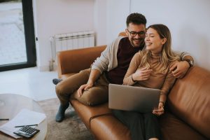 A young couple laughing while on a call with a mortgage broker to secure their first-time buyer mortgage