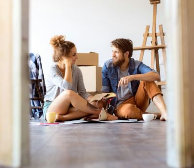 Two first time buyers sitting on the floor in their new house with moving boxes behind them