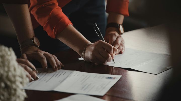 A woman in a long sleeve orange shirt signing mortgage documents