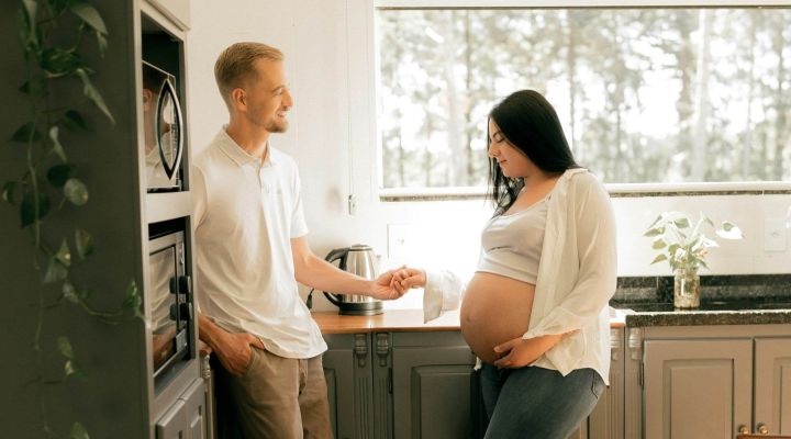 Pregnant woman standing in the kitchen holding her partners hand