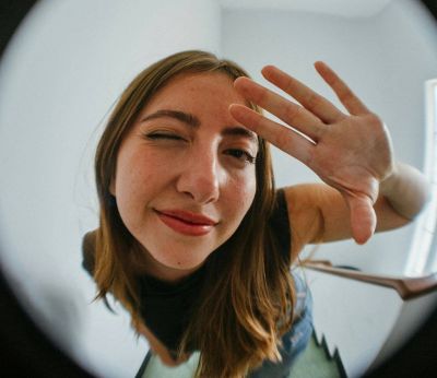 Woman holding up her hand and winking through a door's peephole