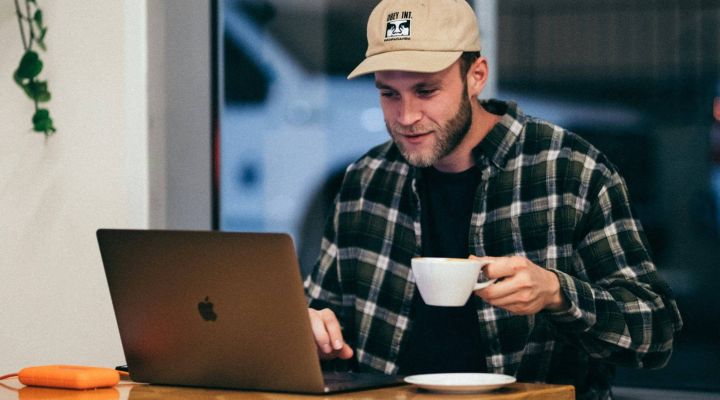 A man working on his laptop in a cafe while drinking a cup of coffee