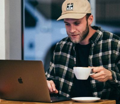 A man working on his laptop in a cafe while drinking a cup of coffee