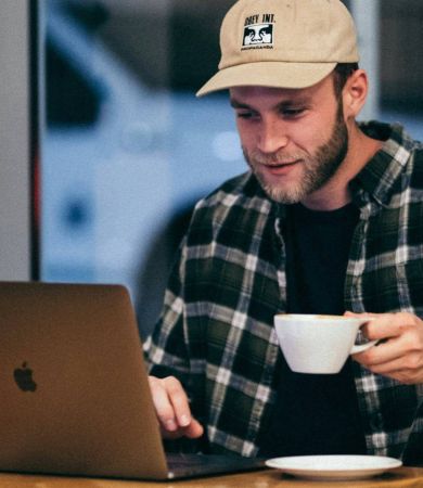 A man working on his laptop in a cafe while drinking a cup of coffee