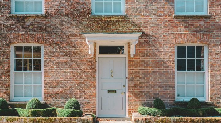 Brick house with ivy scaling the sides and a big grey door in the middle and green bushes outside the front