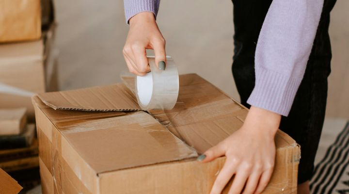 A woman in a purple jumper taping up a moving box on the floor