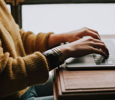 Woman wearing a yellow jumper typing on a laptop