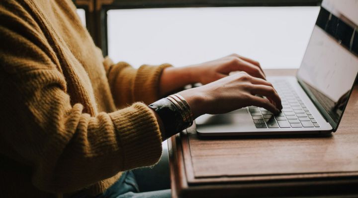Woman wearing a yellow jumper typing on a laptop
