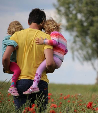 A father carrying his two daughters through a poppy field