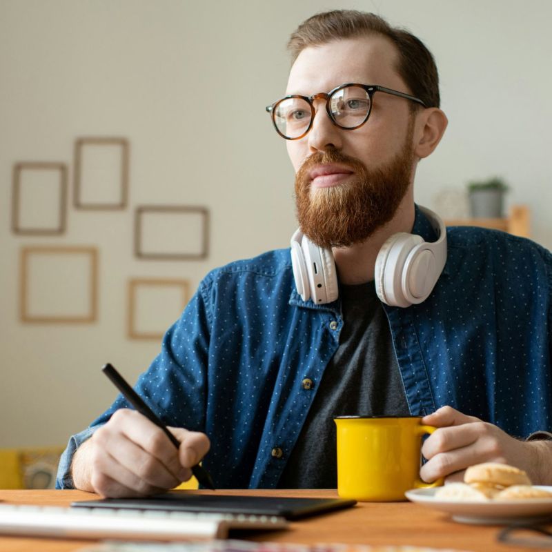 Young creative self-employed professional having a coffee while holding stylus over tablet